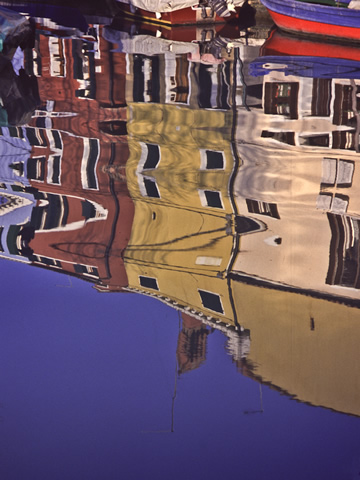 The houses of Burano, reflected here in one of its quiet fishing canals, are each painted in a different super-saturated color with fantastically mismatching colors on the shutters and trim.
